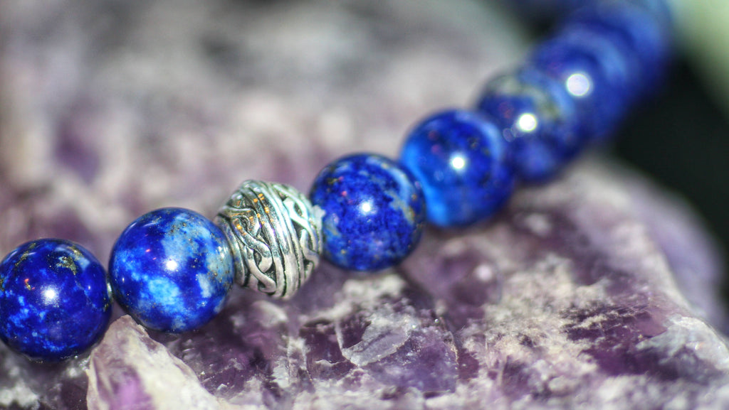 Blue gemstone beads with a silver-tone decorative spacer resting on purple stone.