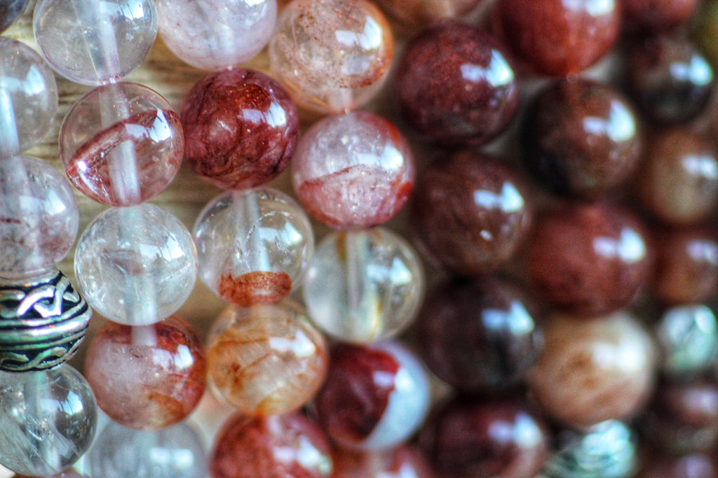 Clear gemstone beads with orange-red inclusions and a silver-tone Celtic knot spacer.